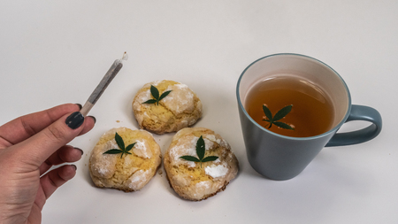 Homemade cupcakes (cake) with medical marijuana and a cap of tea with marijuana leaves on white background. Cannabis joint in woman handの写真素材
