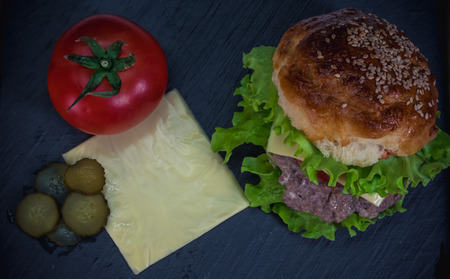 Homemade cheeseburger with a slice of cheese and tomato on a dark gray plate. Tasty and hearty burger.の写真素材