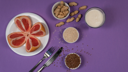 Concept diet - healthy food with grapefruit, peanut, sesame, flax seeds on purple background. White...