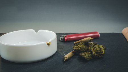 Marijuana buds and joint lie on a dark gray background. Marijuana is medicine. White ashtray and ligter near cannabisの写真素材