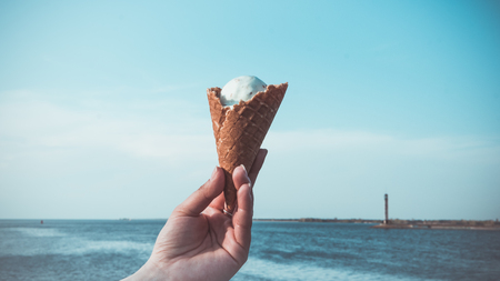 The person holding ice cream in his hand. Calm sea on the background