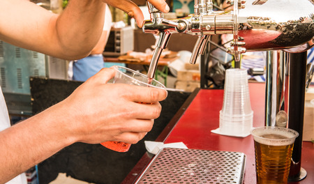 The male bartender pouring beer into a glass close-up. Street food. A glass with cold beer in the bartender's handsの写真素材