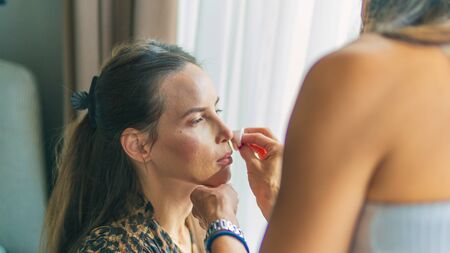 Makeup artist doing professional makeup for young woman. Woman applying by professional make up master.Beautiful model girl indoors.の写真素材