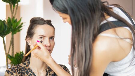 Makeup artist doing professional makeup for young woman. Woman applying by professional make up master.
Beautiful model girl indoors.の写真素材