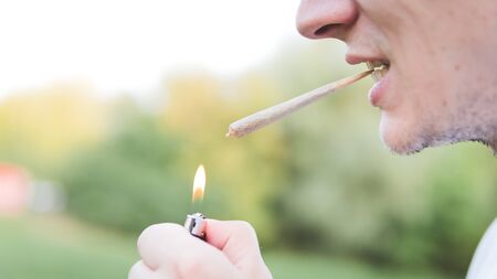 The young person smoking medical marijuana joint outdoors. The young man smoke cannabis blunt, close-up. Cannabis is a concept of herbal medicine.の写真素材
