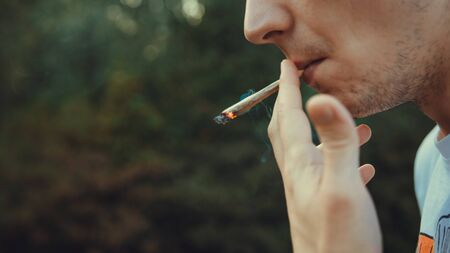 The young person smoking medical marijuana joint outdoors. The young man smoke cannabis blunt, close-up. Cannabis is a concept of herbal medicine.の写真素材
