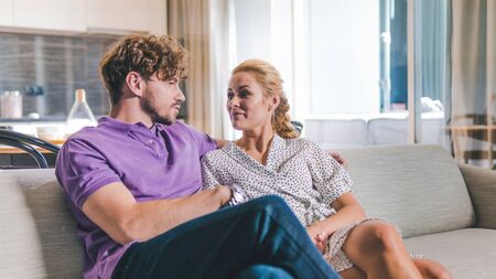 Millennial couple in love relaxing together on sofa at home. Happy couple looking to each other and laugh. Focus on girl and manの写真素材