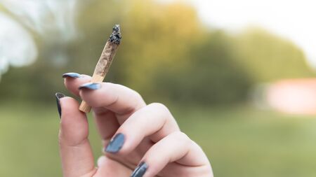 Close-up of females hands holding marijuana joint, smoking cannabis blunt outdoors. Cannabis is a concept of herbal medicineの写真素材