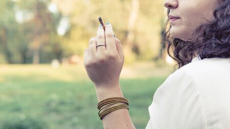 The young person smoking medical marijuana joint outdoors. The young woman smoke cannabis blunt, close-up. Cannabis is a concept of herbal alternative medicine.の写真素材