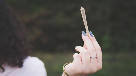 Close-up of females hands holding marijuana joint, smoking cannabis blunt outdoors. Cannabis is a concept of herbal medicineの写真素材