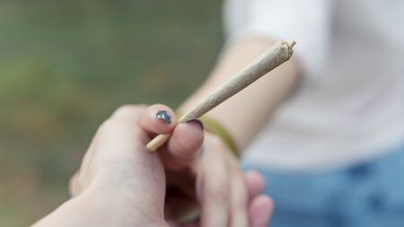 Close-up of females hands holding marijuana joint, smoking cannabis blunt outdoors. Cannabis is a concept of herbal medicineの写真素材