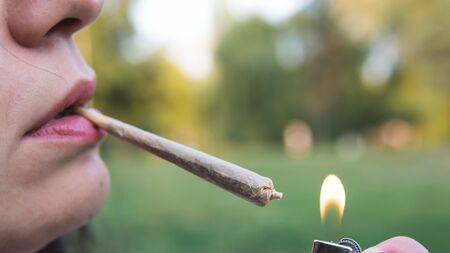The young person smoking medical marijuana joint outdoors. The young woman smoke cannabis blunt, close-up. Cannabis is a concept of herbal alternative medicine.の写真素材
