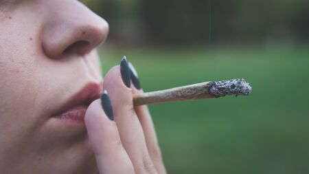 The young person smoking medical marijuana joint outdoors. The young woman smoke cannabis blunt, close-up. Cannabis is a concept of herbal alternative medicine.の写真素材