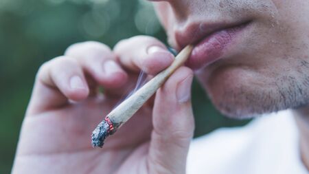 The young person smoking medical marijuana joint outdoors. The young man smoke cannabis blunt,...