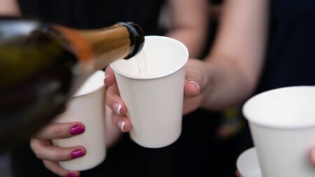 Young woman pouring champagne into glass, close-up outdoors. Young people celebrating with champagne at party outdoors. Concept of hen-party or corporateの写真素材
