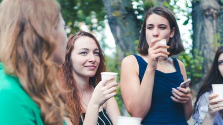Group of girlfriends toasting with champagne in paper glass. Young people celebrating with champagne at party outdoors. Concept of hen-party or corporateの写真素材