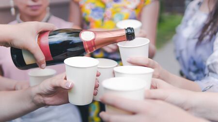 Young woman pouring champagne into glass, close-up outdoors. Young people celebrating with champagne at party outdoors. Concept of hen-party or corporateの写真素材