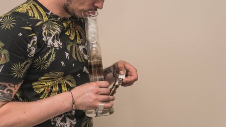 The young person smoking medical marijuana with bong, indoors. The young man smoke cannabis close-up. Cannabis is a concept of herbal medicine.の写真素材