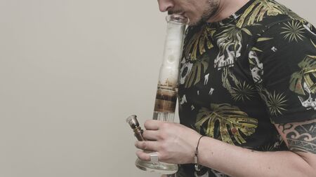 The young person smoking medical marijuana with bong, indoors. The young man smoke cannabis close-up. Cannabis is a concept of herbal medicine.の写真素材