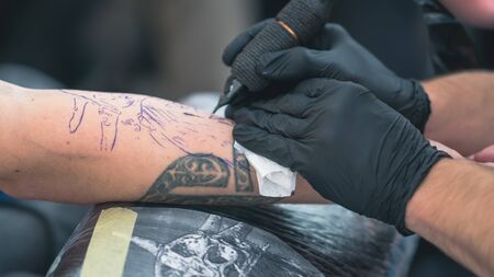 Professional tattoo artist makes a tattoo on a young manâs hand, close-up. Tattoo artist doing tattoo in tattoo salon. Process of making tattoo in tattoo studio.の写真素材