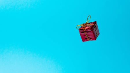 Red gift box with golden ribbon on trendy neon color background, close-up. levitation and copy space. Concept sales, discount price, Christmas and New Year presents and shopping.の写真素材