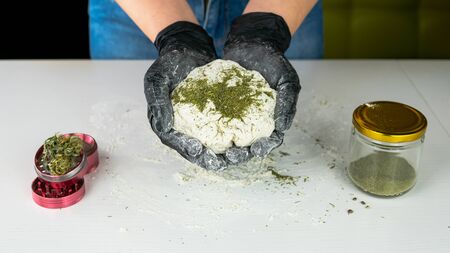 The young female chef preparing to cooking hemp cake or bread. Close-up of fresh dough with cannabis flour. Concept of uses marijuana in a food industryの写真素材