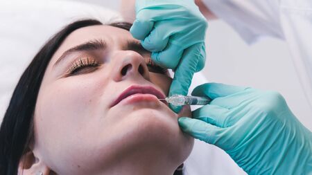 Beautician hands making  injection in  lips. The doctor cosmetologist makes lip augmentation procedure. Concept of beauty salon and plastic surgery clinic.の写真素材