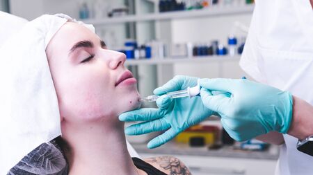 The female beautician doctor making injection in young woman face. The doctor cosmetologist doing facial contouring procedure. Concept of beauty salon and plastic surgery clinic.の写真素材