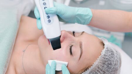 The female cosmetologist makes  a procedure of ultrasonic cleaning face, close-up. Young woman in a...