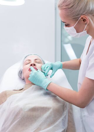The young beautician doctor preparing to making injection in female lips. The doctor cosmetologist makes lip augmentation procedure. Concept of beauty salon and plastic surgery clinic.の写真素材