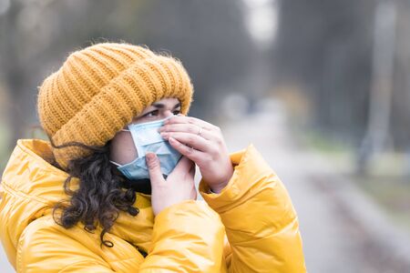 Close-up portrait young europeans woman in protective disposable medical face mask walking outdoors. New coronavirus (COVID-19). Concept of health care during an epidemic or pandemicの写真素材