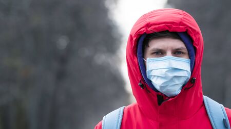 Close-up portrait young europeans man in protective disposable medical face mask walking outdoors....