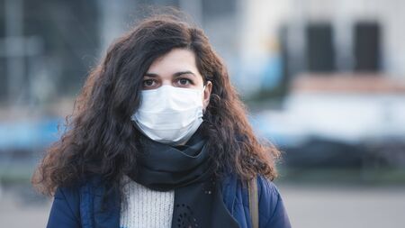 Close-up portrait young europeans woman in protective disposable medical face mask walking outdoors. New coronavirus (COVID-19). Concept of health care during an epidemic or pandemicの写真素材
