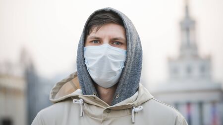 Close-up portrait young europeans man in protective disposable medical face mask walking outdoors....