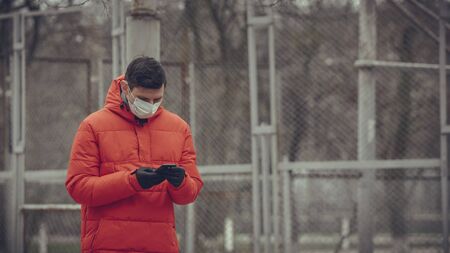 Close-up portrait young europeans man in protective disposable medical face mask walking outdoors....
