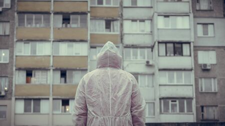 The man in protective chemical suit stands back and looks at the building, outdoors. New coronavirus (COVID-19). Concept of health care during an epidemic or pandemicの写真素材