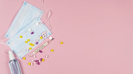 Protective medicine mask, antiseptic thermometer and pills on pink background, flat lay. Concept of doctor table and health care. Top view, copy spaceの写真素材