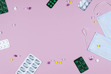 Protective medicine mask, antiseptic thermometer and pills on pink background, flat lay. Concept of doctor table and health care. Top view, copy spaceの写真素材