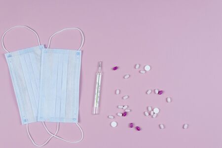 Protective medicine mask, thermometer and pills on pink background, flat lay. Concept of doctor...