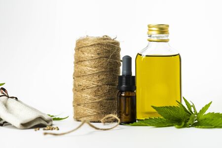 Glass bottles with CBD essential oil, medical marijuana leaf, seeds and hemp thread on white background, close-up. Concept of using cannabis in fabric production and herbal medicineの写真素材