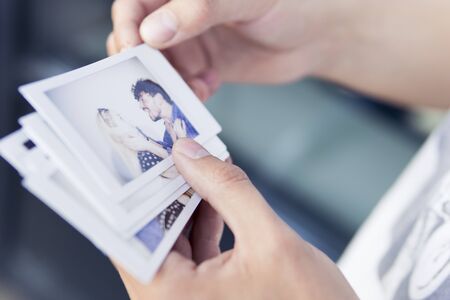 Close-up of man holding in the hand printed photos with picture of young couple. Concepts of happy memories, romantic and loveの写真素材
