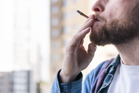 Close-up of male hand holding and smoking marijuana joint or cigarette outdoors. Cannabis is a concept of herbal and alternative medicineの写真素材