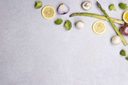 Group of organic fresh vegetables - green asparagus, broccoli, mushrooms on grey background, flat lay. Concept of  healthy vegetarian food, diet and home cooking. Top view, copy space.の写真素材