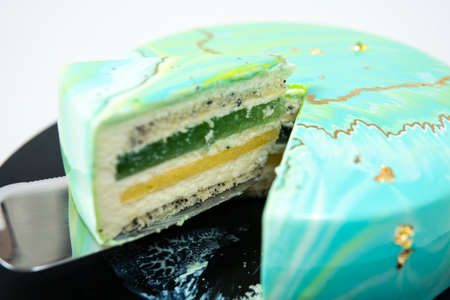 Close-up slice of mousse cake covered blue and green mirror glaze on spatula. French dessert. Frozen mirror icing on the cake. Baking and confectionery concept. White backgroundの写真素材