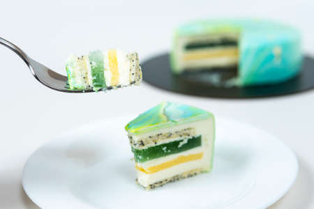 Close-up eating slice of mousse cake covered blue and green mirror glaze. French dessert. Frozen...