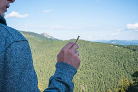Close-up of young man smoking marijuana joint outdoors. Hemp blunt in the male hand. Cannabis is a...