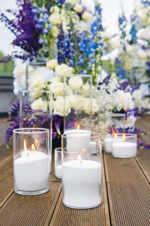Close-up of white candles on wedding reception with white, blu and violet flower, outdoors. Elegant luxury wedding decoration composition on ceremony place or photo zoneの写真素材