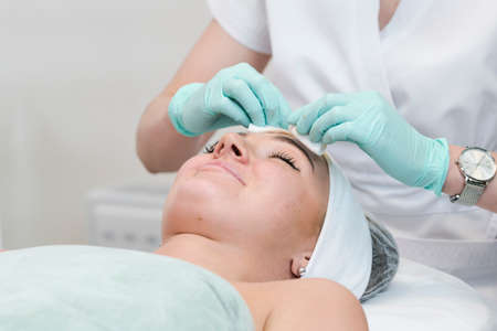 The young female client of cosmetic salon having a face cleaning procedure. The doctor cosmetologist cleaning skin with sponge. Concepts of skin care and beauty salon or clinic.の写真素材