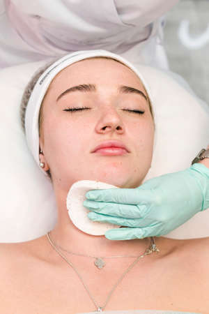The young female client of cosmetic salon having a face cleaning procedure. The doctor cosmetologist cleaning skin with sponge. Concepts of skin care and beauty salon or clinic.の写真素材