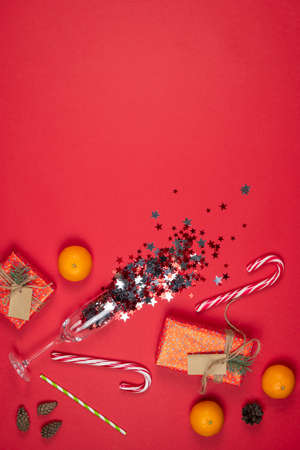Glass of champagne with confetti, New Year and Christmas presents, handmade gift boxes wrapped with red paper and decorated fir tree branches, flat lay. Copy space. Concepts of greeting card. Top view.の写真素材